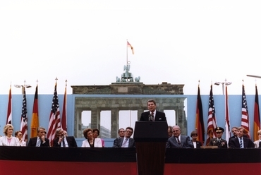 Ronald Reagan beszédet mond a fal előtt 1987-ben. A díszletfal kivágásában a Brandenburgi kapu látható. Kép: White House Photographic Office - Ronald Reagan Presidential Library, ID C41244-9.