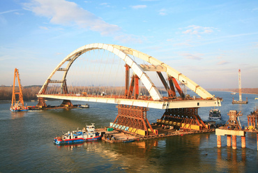 Az építés legfontosabb napja 2006 december 6-án: a parti szerelőtérről végleges helyére úszik az elkészült középső nyílás. A bárkákkal és vontatókkal 12 ezer tonna feletti tömege a Dunán valaha mozgatott legnagyobb tárgy.  Forrás: Hídépítő Speciál Kft.