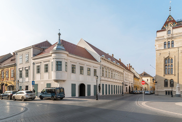 A Szentháromság-tér másik új épülete nem egy évtizedek óta üres, vagy torz helyen épült. Az itteni diplomata lakóház Jánossy György és Laczkovics László közös munkájaként 1981-re készült el, a háborút követő foghíjbeépítések egyikeként. 2022-es lebontása jelentős szakmai tiltakozás ellenére történt.
