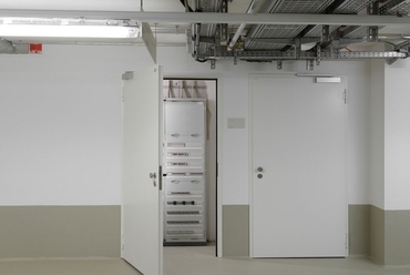 A mélygarázsból közelíthetők meg a műszaki helyiségek, amelyek nyílásait vékonyfalcos, fehérre festett acéllemez ajtók zárják le. Az ajtók tűz- és füstgátló nyílászárók.