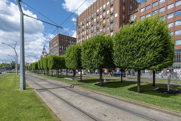 A Kiskörút szögletesre nyírt zöld lombkoronái mellett siklanak napi mint nap a 47-49-es villamosok sárga kubusai. A fák lombkoronaformái harmodizálnak a Madách tér vöröstéglás épülettömegeivel, rendezetten simulva a Kiskörút Deák Ferenc tér és Astoria közötti szakaszába.  / Lépték Tájépítész Iroda
