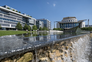 Hatalmas vízfelület, ami a lerombolt Blaha Lujza téri színház stilizált homlokzatát rejti, melyet színpadszerű hajóimitáció szel keresztbe. // Bajor Gizi park
